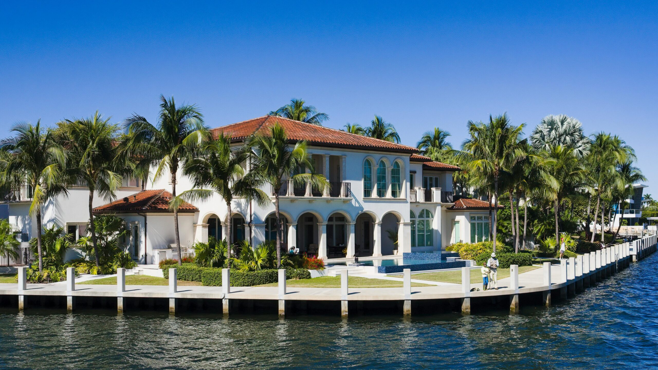 a white two story house surrounded palm trees and body of water