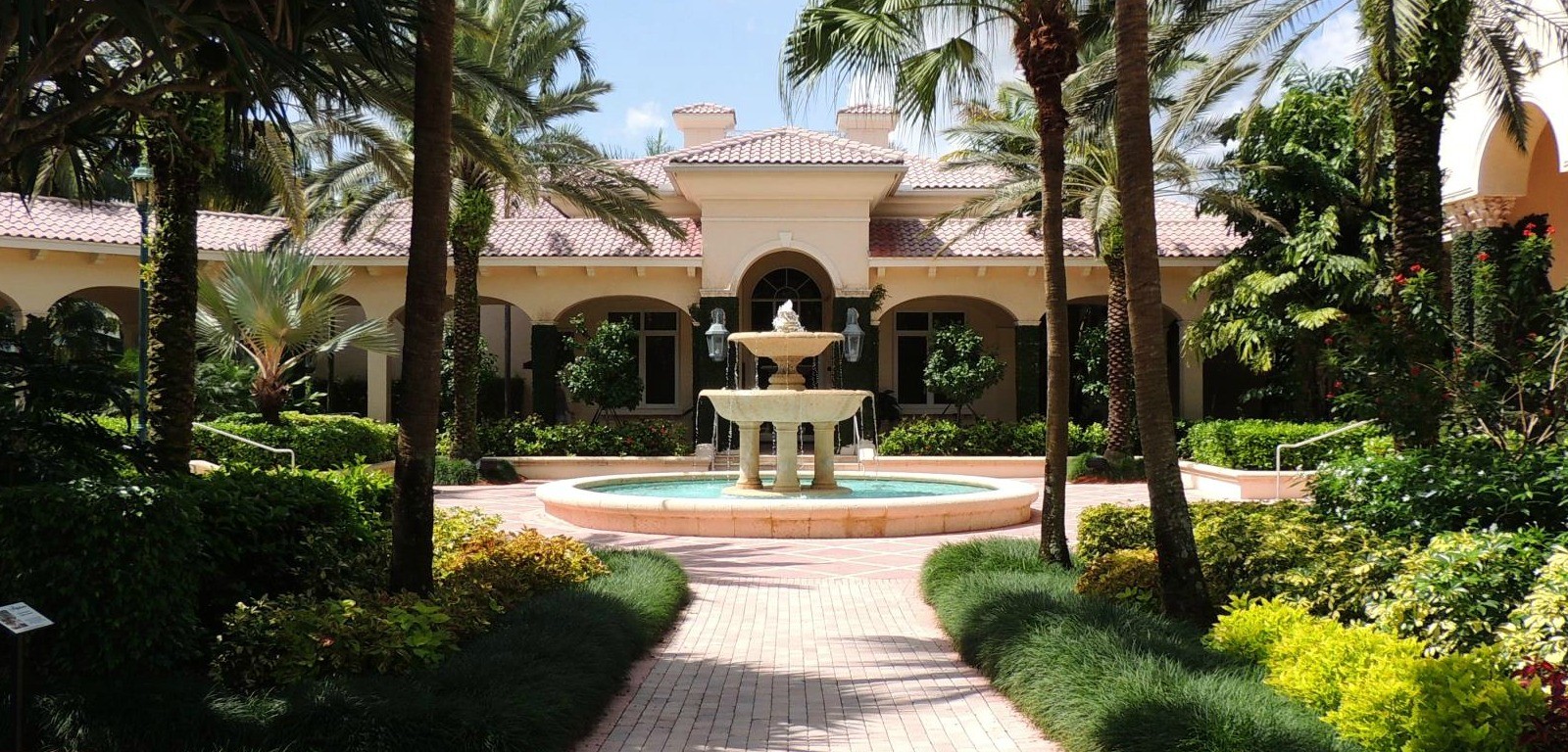 a fountain in the middle of a beautiful garden with plants and palm trees